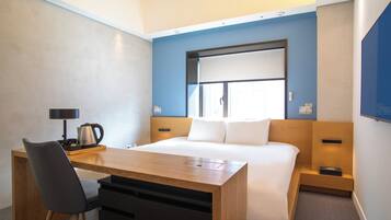 Habitación de hotel con cama, escritorio, silla, cafetera y televisor.