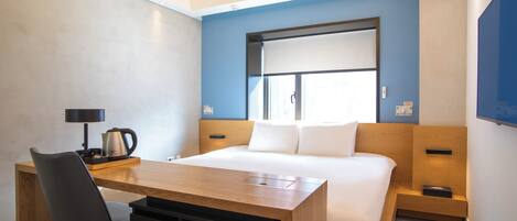 Habitación de hotel con cama, escritorio, silla, cafetera y televisor.