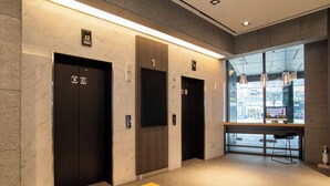 A modern elevator area with three elevators, numbered 1 to 12, and a glass wall with a view of the outside. - HOP INN Seoul Myeongdong (Seoul)