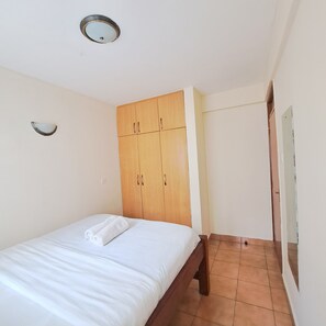 Ein Schlafzimmer mit einem Bett, einem Holzschrank und einer kleinen Wandleuchte.