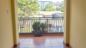 Een gang die uitkomt op een balkon met uitzicht op gebouwen en bomen.