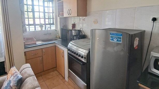 Een compacte keuken met een fornuis, oven en een koelkast. Er is een raam met uitzicht op groen, en een klein aanrecht met een spoelbak.