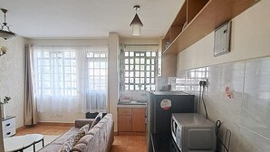 Een kleine keuken met een eethoek, met een bank, een tafeltje en een koelkast.