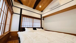 A bedroom with a wooden ceiling, a large window with a grid pattern, and a bed with white bedding. - Yuharizuki (Kyoto)