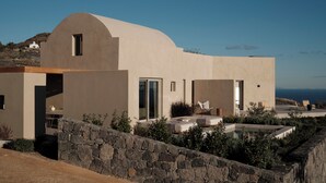 A modern house with a curved roof, a stone wall, and a pool area with lounge chairs. - Geranium Villa with Private Pool, Epos Villas Imerovigli (Thira - Santorini)