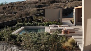 A modern outdoor pool area with a stone wall, a lounge with seating, and a view of a hillside. - Geranium Villa with Private Pool, Epos Villas Imerovigli (Thira - Santorini)