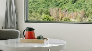 A room with a round white table, a red coffee pot, and a tray with cups and a thermos. A window with a view of a forest is visible. - Longtian (Luye)