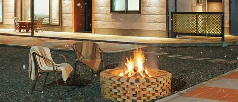A fire pit with logs, surrounded by outdoor seating and a building with large windows.