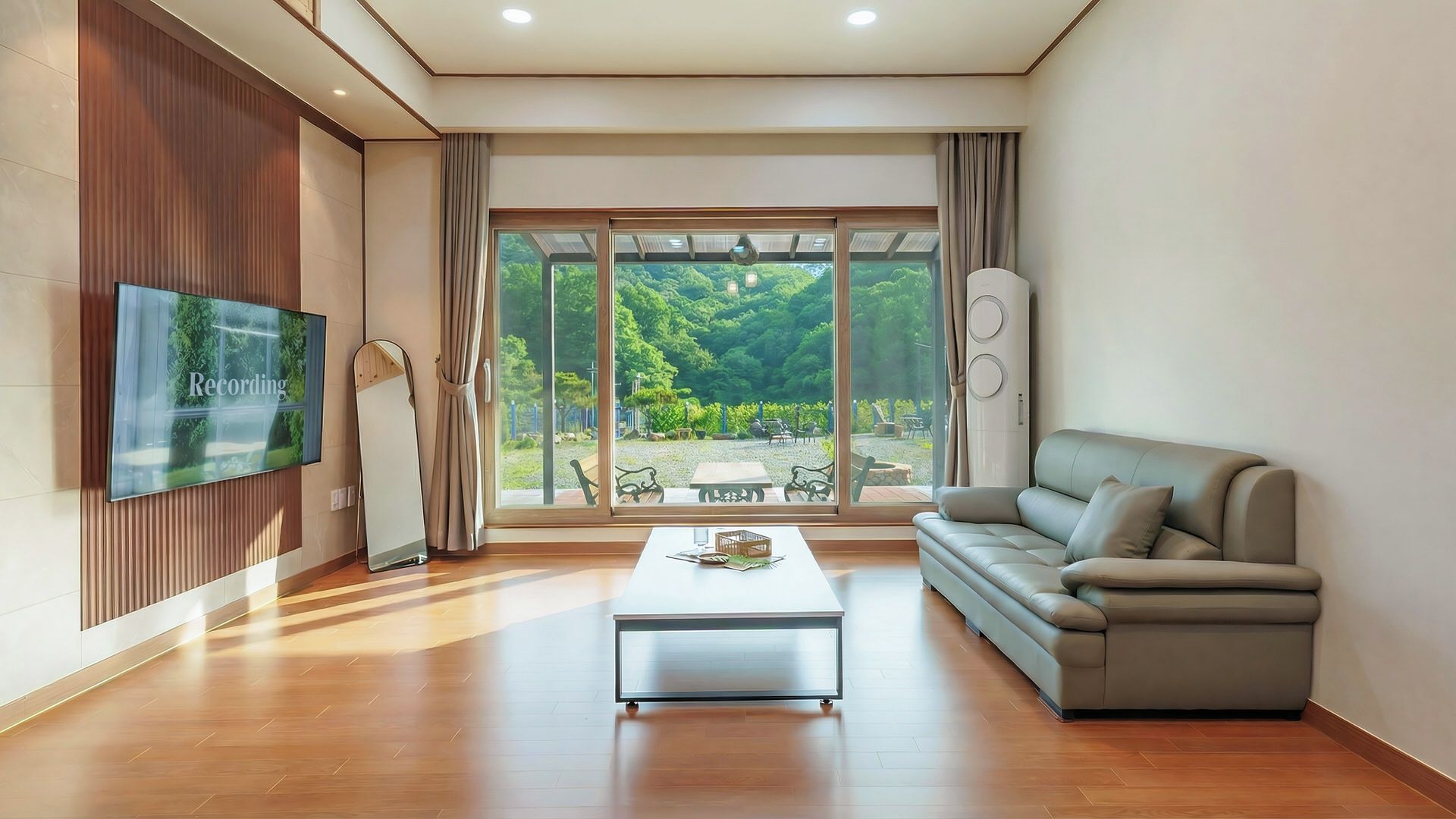 A modern living room with a flat-screen TV, a sofa, a coffee table, and a large sliding glass door leading to an outdoor area.