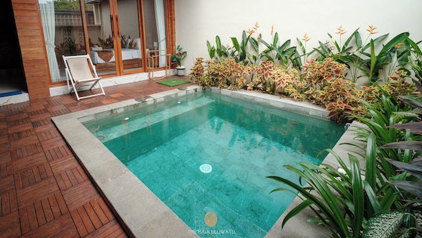 Una piscina con cubierta de madera, rodeada de plantas tropicales y un ventanal que da a un balcón.