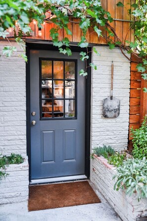 A dark gray door with a window, a potted plant, and a shovel on the wall. - Midcentury Gem with Beautiful Outdoor Kitchen (Wheat Ridge)