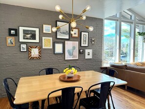 A dining area with a wooden table, black chairs, a chandelier, and framed pictures on the wall. - Midcentury Gem with Beautiful Outdoor Kitchen (Wheat Ridge)