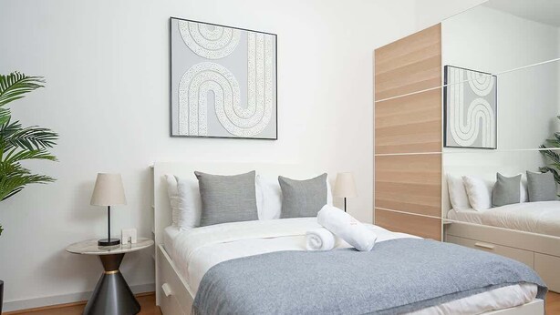 Et moderne hotelværelse med seng, natbord, lampe og spejl.