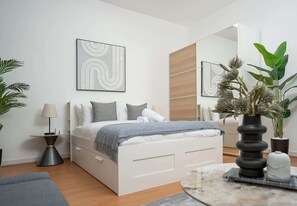Un dormitorio moderno con cama, mesita de noche, lámpara y un espejo grande.