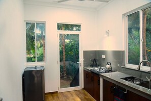 A compact kitchen with a gas stove, sink, and a small refrigerator. There are two windows providing views of greenery outside. - Dady`s Place `63` German standard with Singalese charm - beach in 2 min (Hikkaduwa)