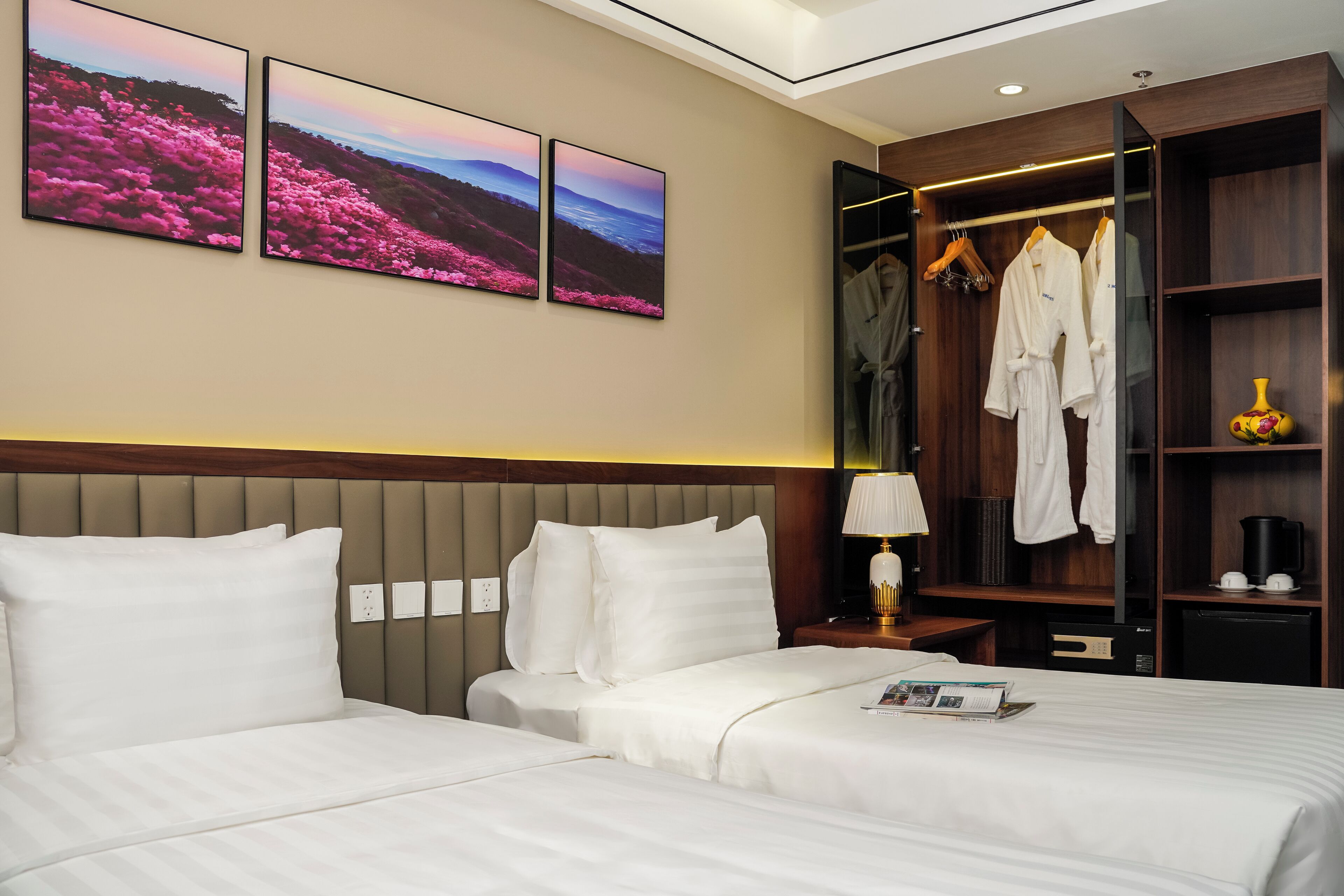 A hotel room with two beds, a wardrobe, and artwork on the wall.