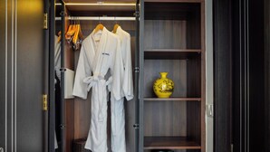 A walk-in closet with white robes hanging on a rack, a wicker basket, and a shelf with a yellow vase and black kettles. - Blubiz Hotel 6 (Hanoi)