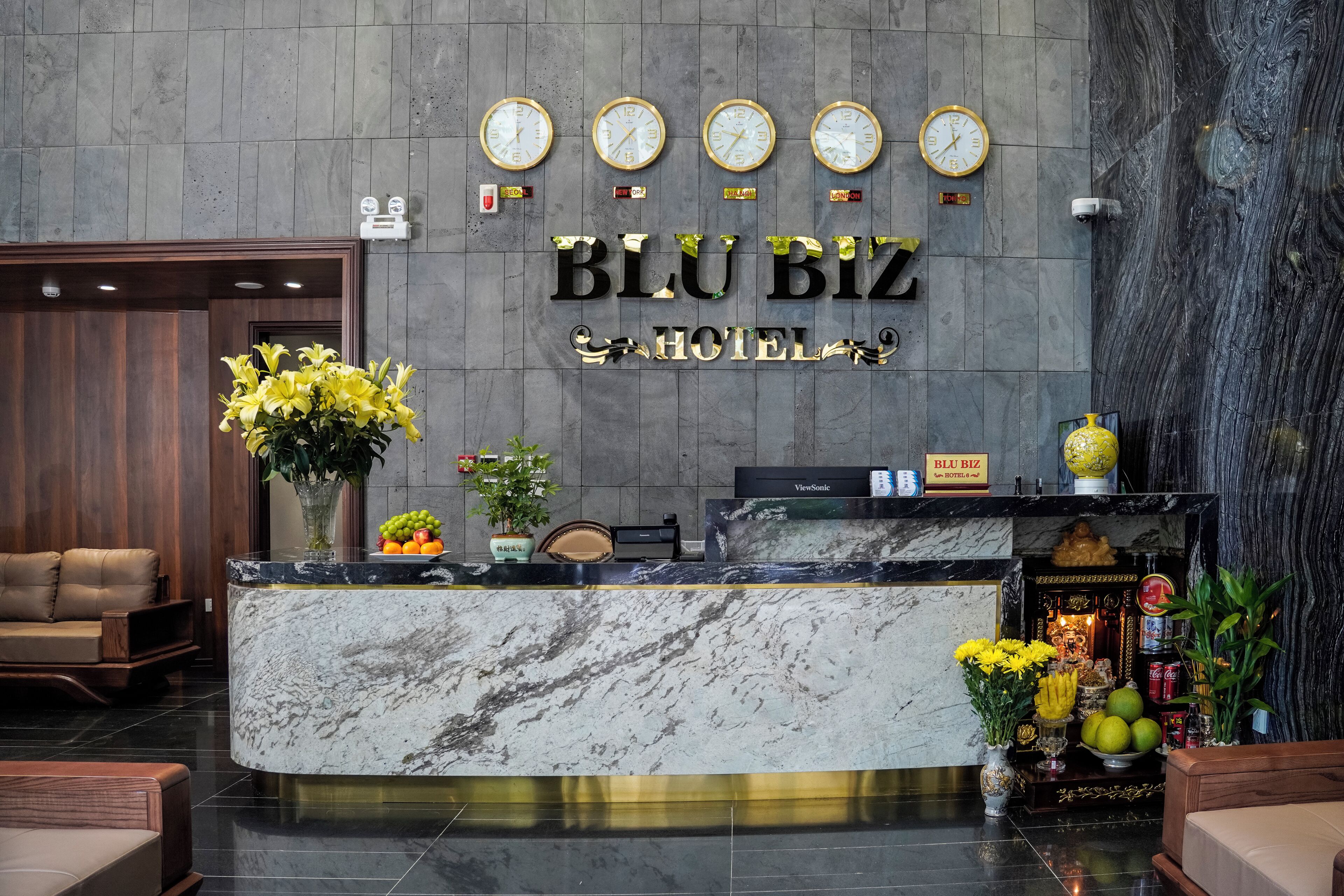 A reception desk with a marble top, a clock, and a sign that reads "Blu Biz Hotel".