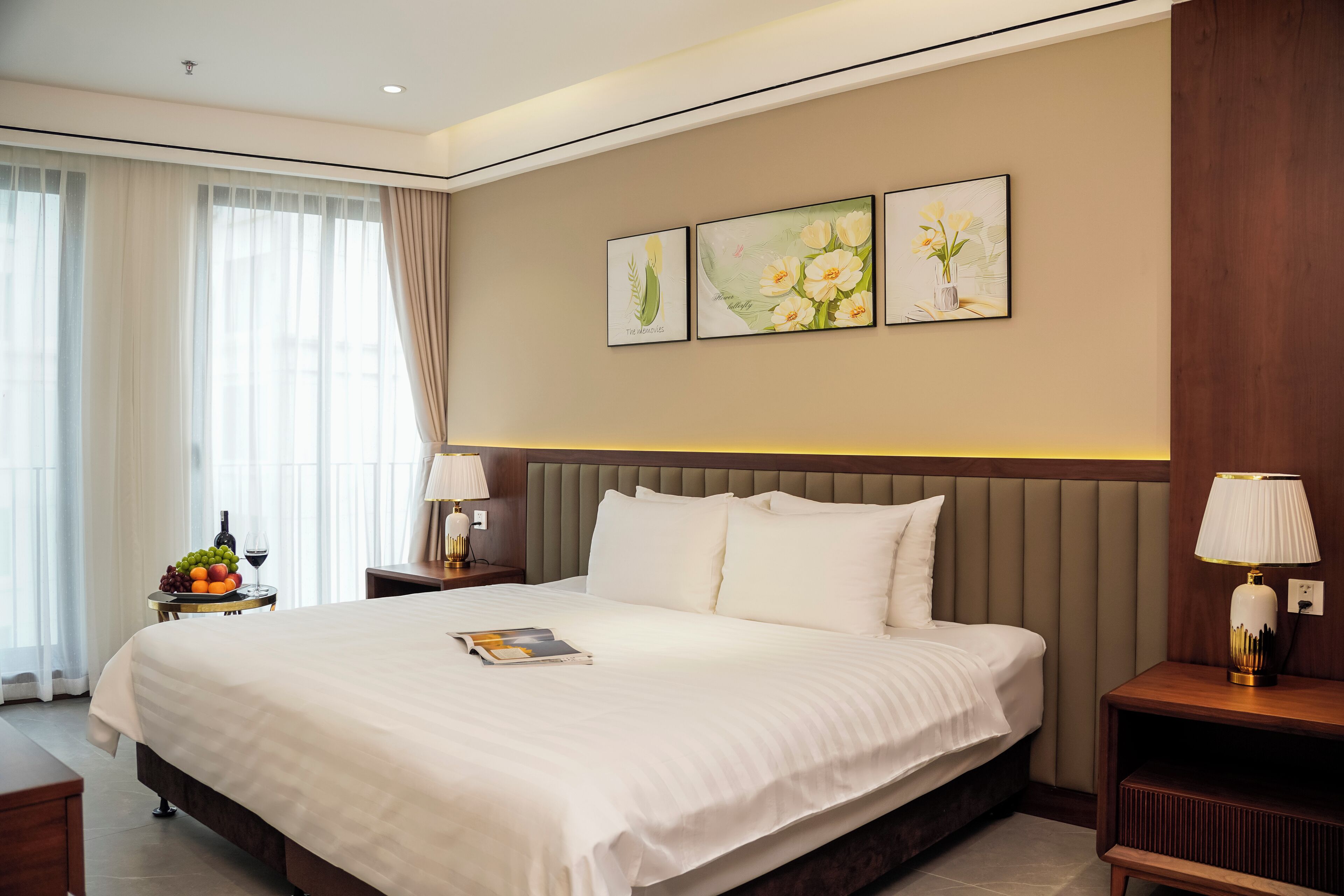 A hotel room with a large bed, a nightstand with a lamp, a fruit bowl, and a magazine on the bed.