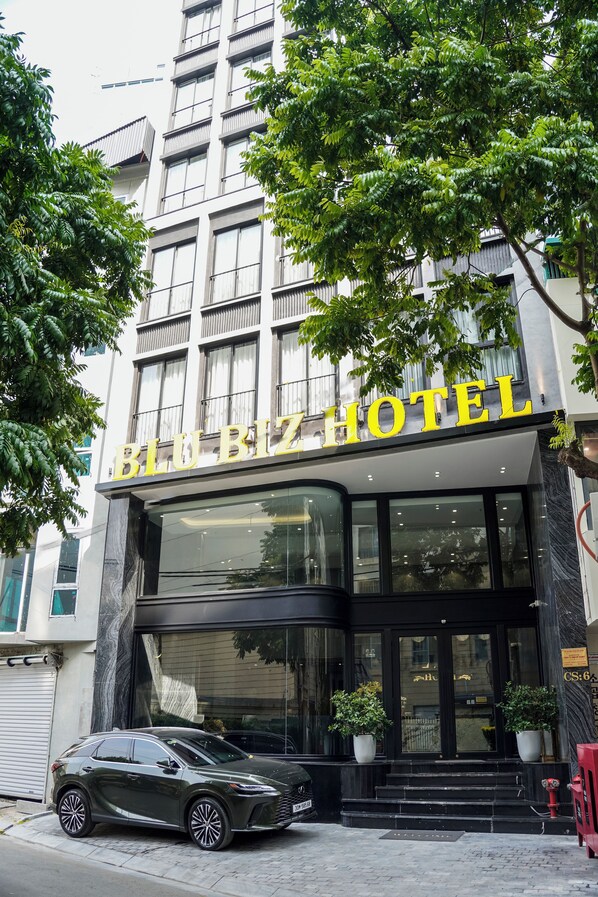 A hotel entrance with a modern facade, large windows, and potted plants at the entrance. - Blubiz Hotel 6 (Hanoi)