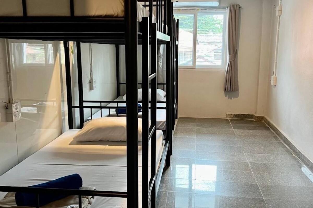 A dormitory room with bunk beds, a window with curtains, and an air conditioning unit on the wall.