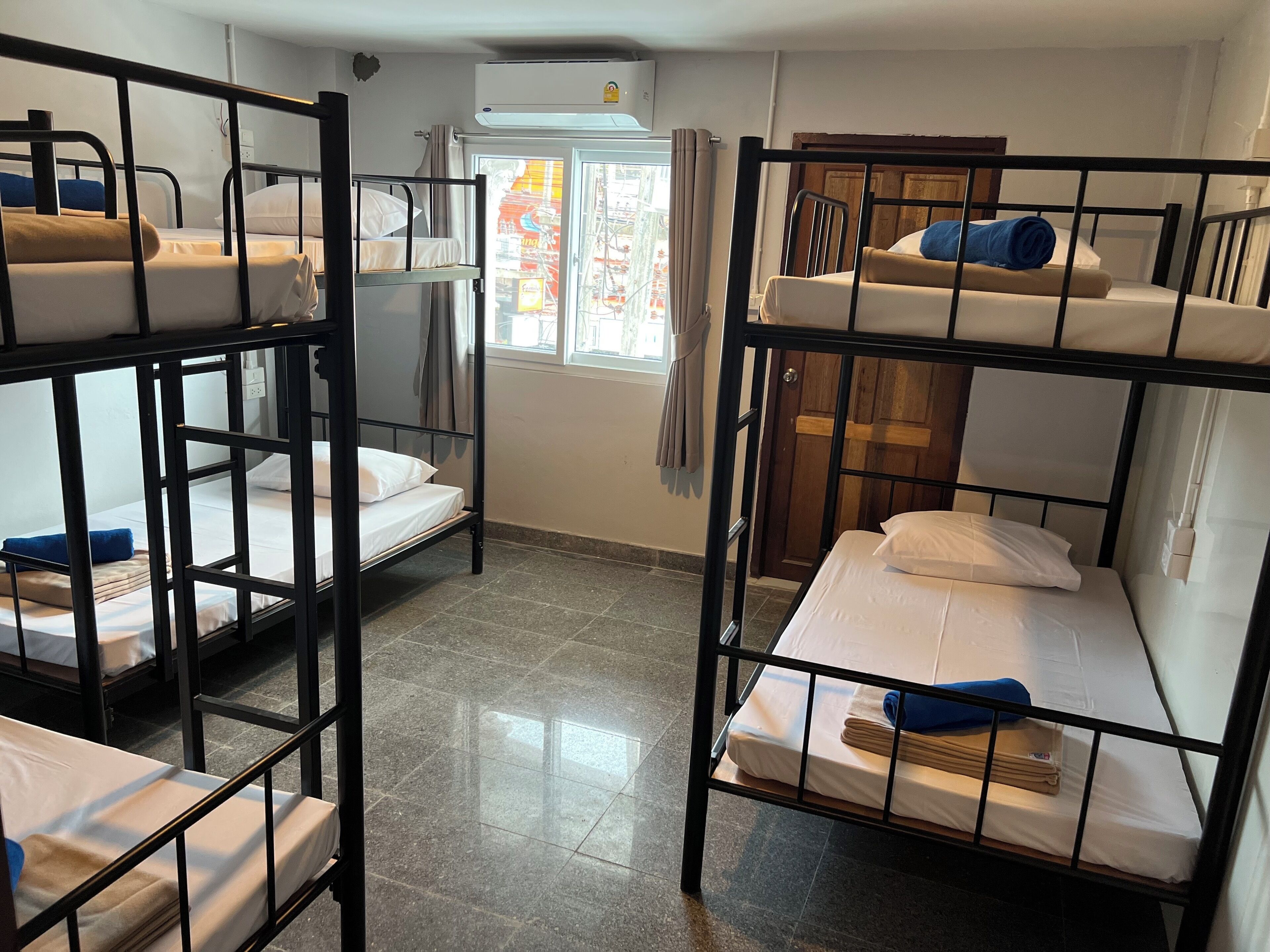 A dormitory room with bunk beds, a window with curtains, and a tiled floor.