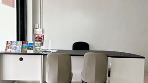 A modern office space with a desk, two chairs, a white pendant light, and a window with a view. - YP Hostel (Koh Samui)