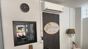 A room with a wooden table, a clock, a wall-mounted air conditioner, a decorative sign, a lamp, and a small potted plant. - YP Hostel (Koh Samui)