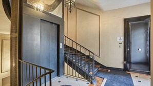 A modern interior with a staircase, a chandelier, and a door with a sign. - Sumptuous apartment Louvre/Palais Royal (Paris)