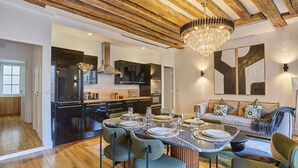 A modern kitchen with a central island, wooden ceiling beams, and a chandelier. - Sumptuous apartment Louvre/Palais Royal (Paris)