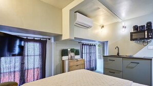 A bedroom with a bed, a wooden nightstand, a desk with a sink, and an air conditioning unit. - Charming air-conditioned studio in the center of Paris (Paris)