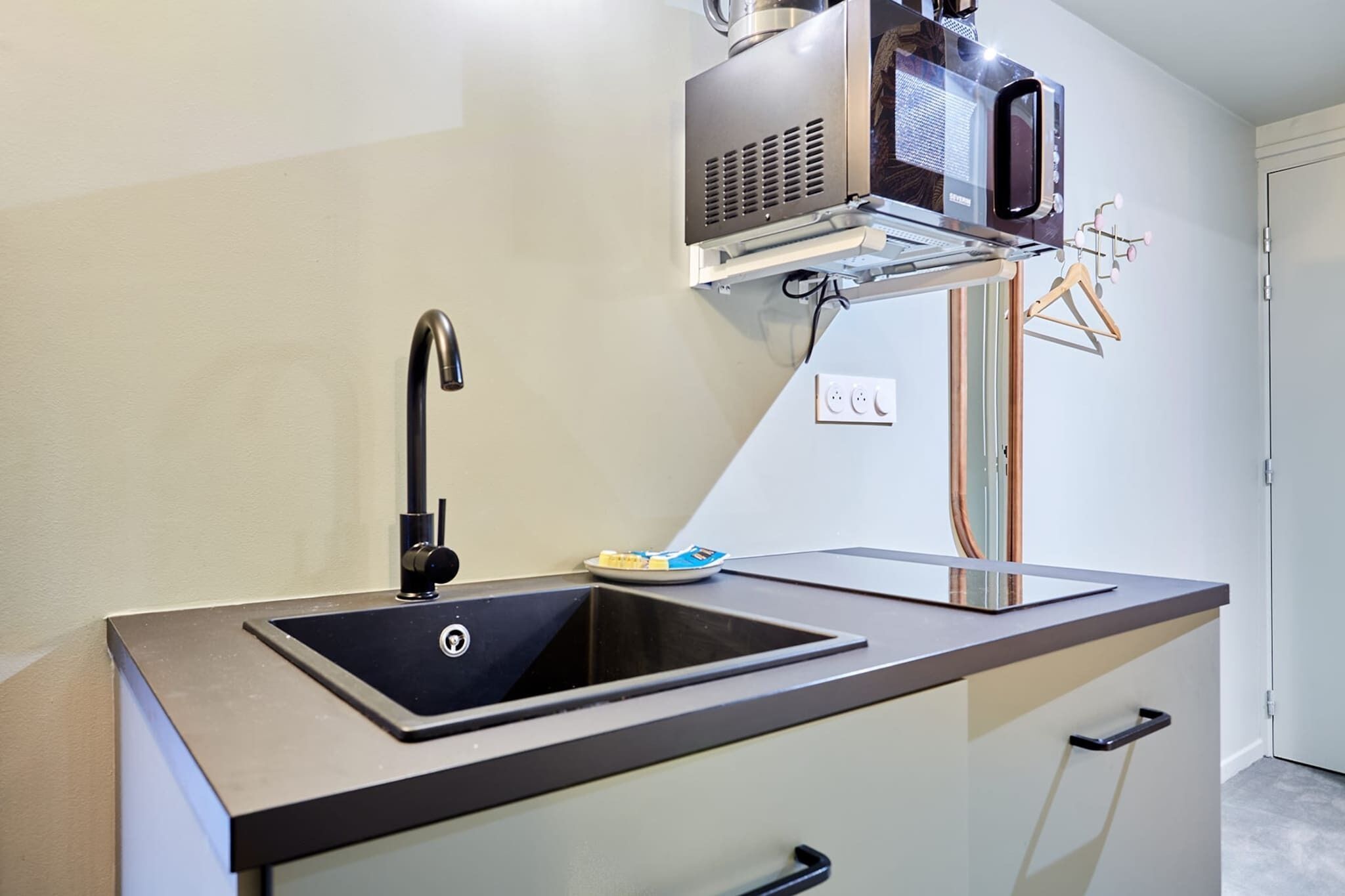 A modern kitchen with a stainless steel sink, a faucet, a microwave, and a small dish rack.