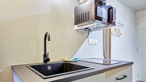 A modern kitchen with a stainless steel sink, a faucet, a microwave, and a small dish rack. - Charming air-conditioned studio in the center of Paris (Paris)