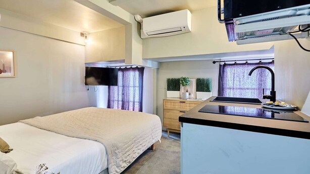A compact hotel room with a bed, kitchenette, and a small window with curtains. - Charming air-conditioned studio in the center of Paris (Paris)