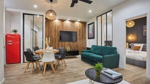 Ein modernes Wohnzimmer mit Fernseher, einem roten Kühlschrank, einem grünen Sofa und einem Essbereich mit Tisch und Stühlen.
