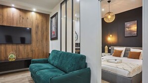 Ein modernes Schlafzimmer mit einem großen Bett, einem grünen Sofa, einem an einer Holzwand montierten Fernseher und einer Wandleuchte.