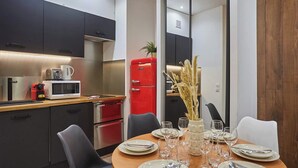 Eine moderne Küche mit dunklen Schränken, einem roten Kühlschrank und einem Essbereich mit einem für vier Personen gedecktem runden Tisch.