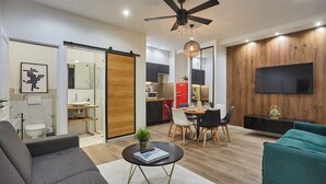 Ein modernes Wohnzimmer mit Sofa, Couchtisch und einem Türkis-farbenen Sofa. Es gibt einen Essbereich mit Tisch und Stühlen. Ein Fernseher ist an der Wand befestigt und ein Deckenventilator ist zu sehen.