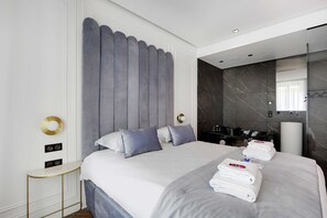 Een moderne hotelkamer met een groot bed, nachtkastje, spiegel en een badkamer met bad.