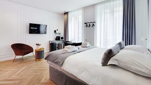 A modern hotel room with a large bed, a flat-screen TV, a desk with a computer, and a chair. - Superb Suite with AC Beaubourg Le Marais (Paris)