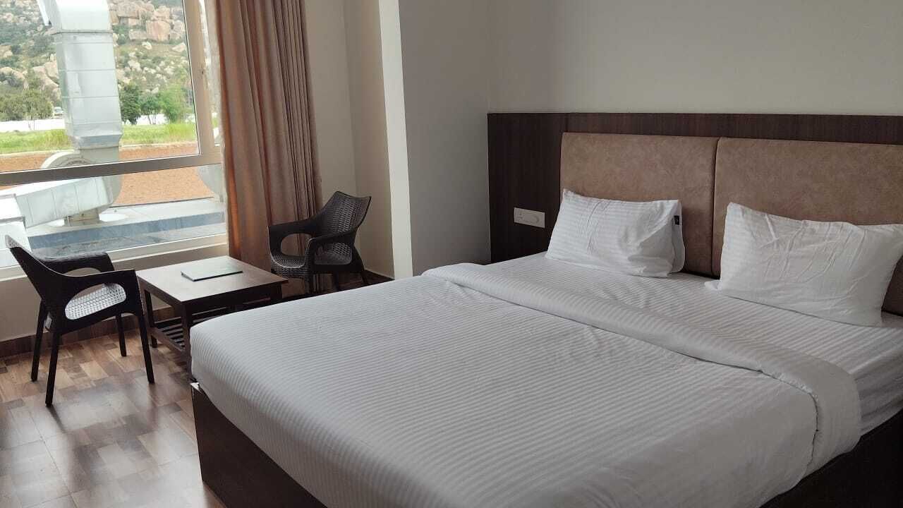 Habitación de hotel con una cama grande, un escritorio y una silla. Se ve follaje verde por la ventana.