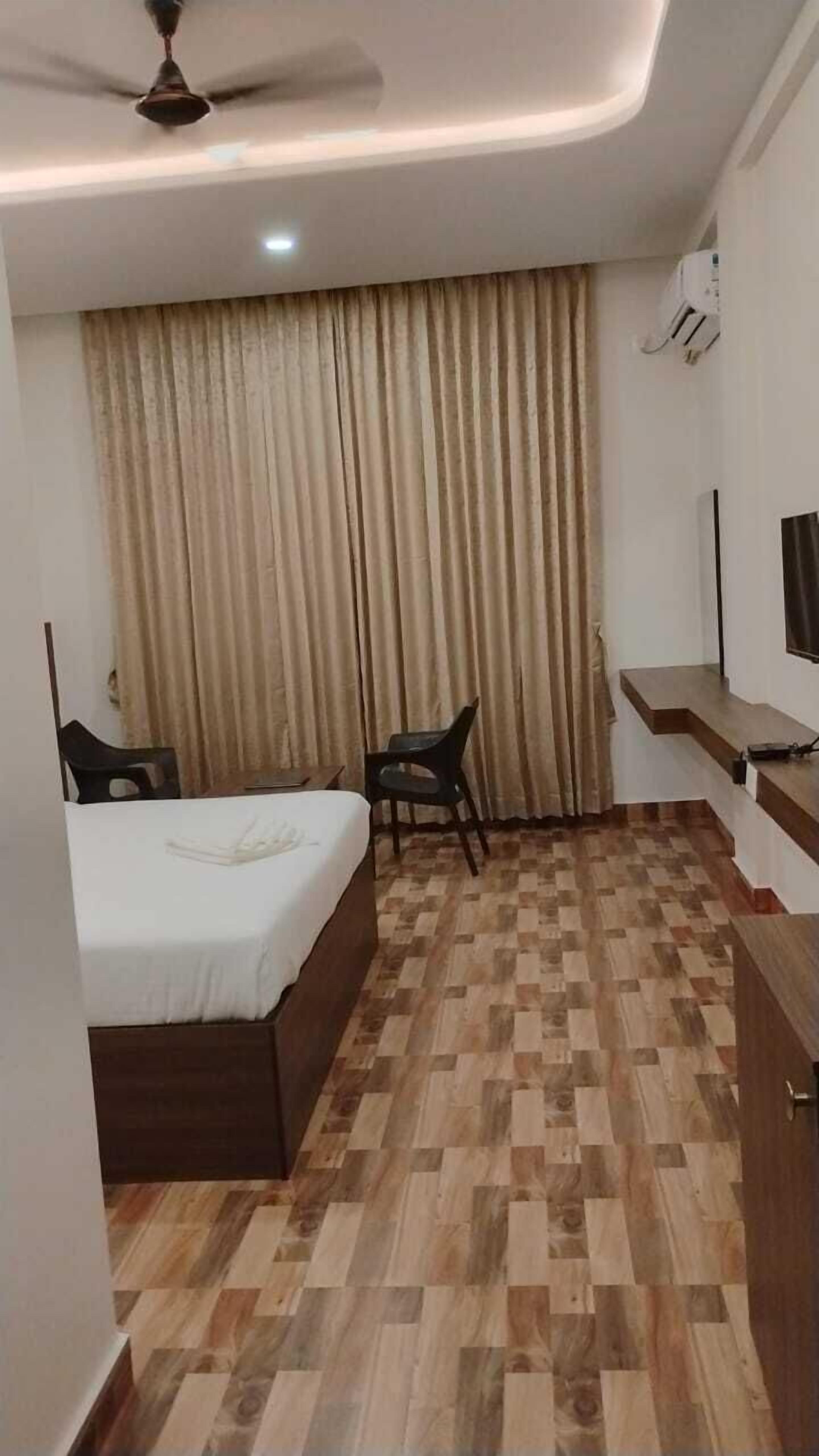 Una habitación de hotel con una cama, dos sillas, un escritorio, un televisor y un ventilador de techo.