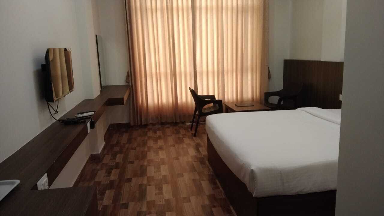 Quarto de hotel com cama, escrivaninha, cadeira, televisão e janela com cortinas.