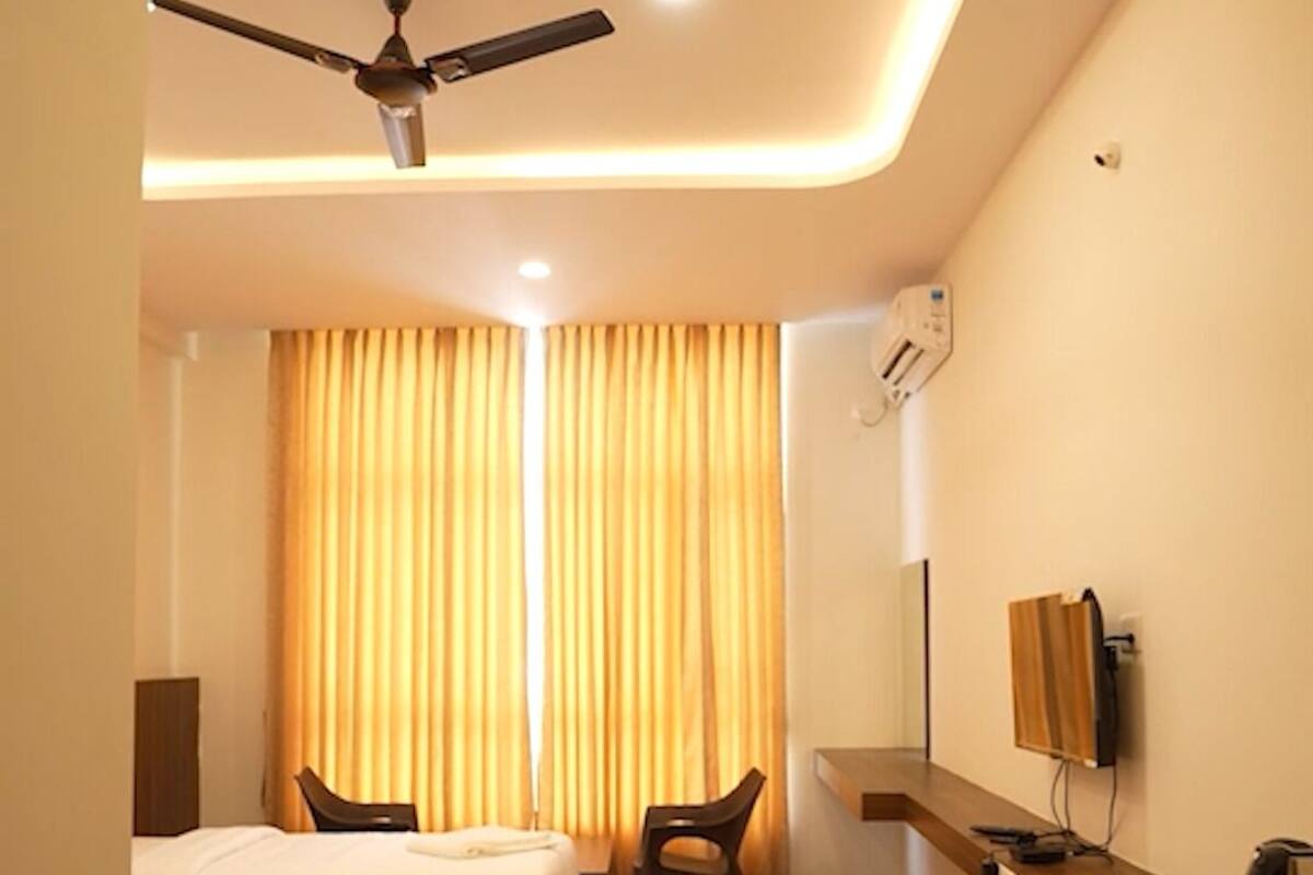 Habitación de hotel con dos camas, un escritorio, una silla, ventilador de techo y televisión.