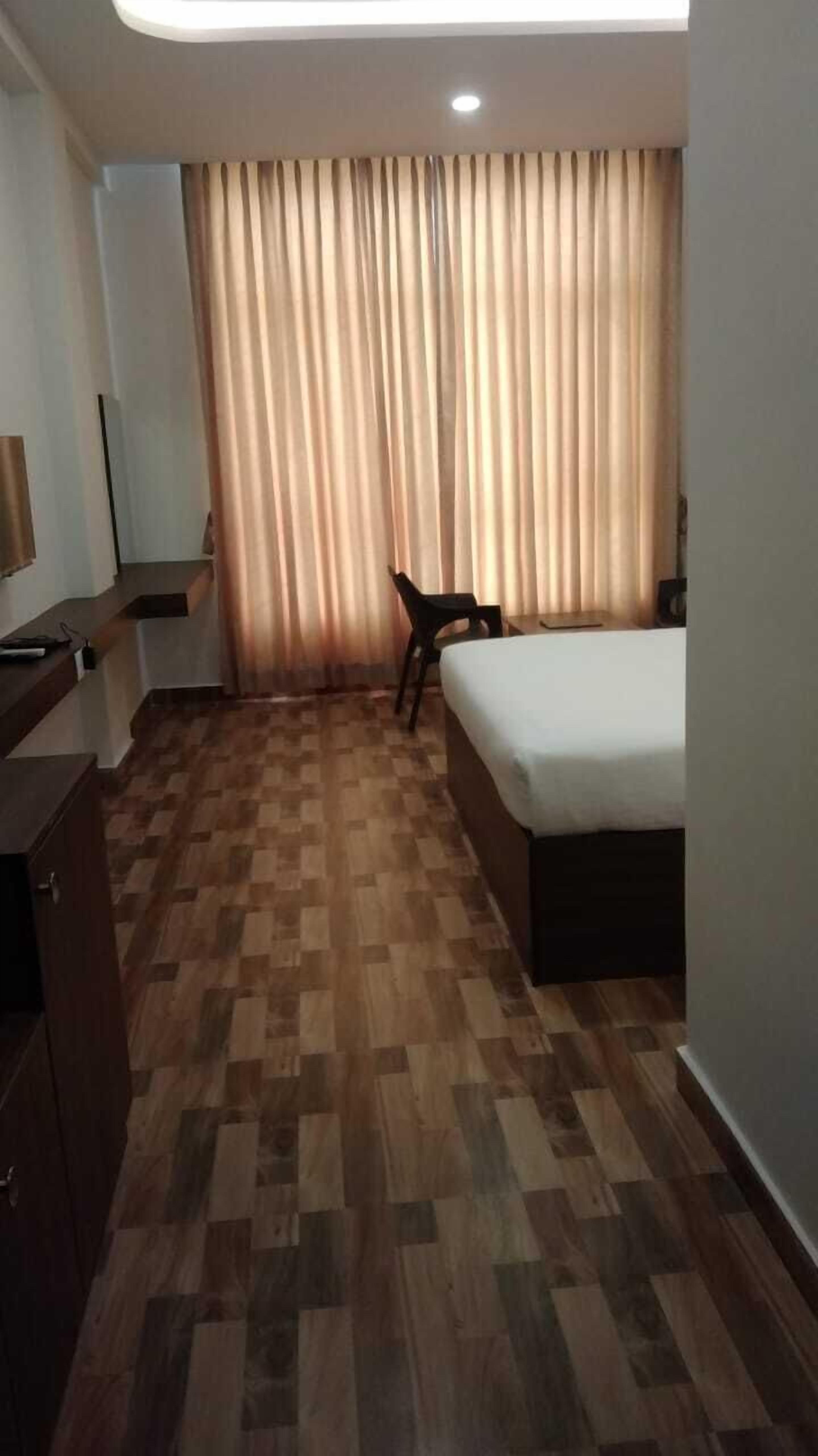 Ein Hotelzimmer mit Bett, Schreibtisch, Stuhl und einem Fenster mit Vorhängen.