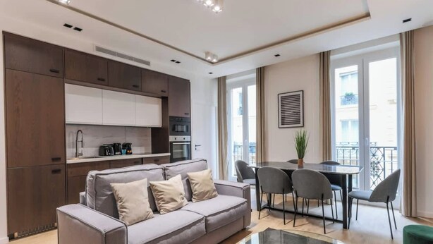 Una sala de estar moderna con un sofá gris, una mesa de centro de vidrio y un comedor con mesa y sillas.