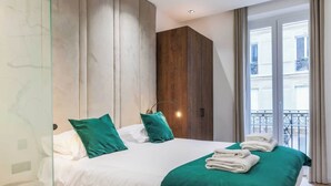Una habitación de hotel moderna con una cama grande, ropa de cama verde, un armario de madera y un balcón con vista a la ciudad.