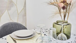 Ein Esstisch, gedeckt mit Tellern, Besteck und einer Vase mit Trockenblumen.