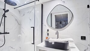 Ein modernes Badezimmer mit einer gläsernen Duschkabine, einem runden Spiegel, einem schwarzen Waschbecken und einer Wand mit Marmorplatten.