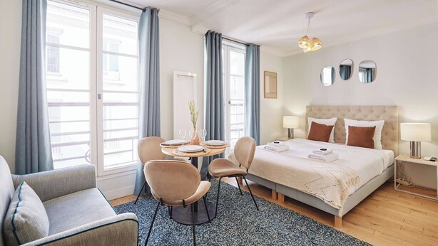 Ein Hotelzimmer mit einem Bett, zwei Stühlen, einem kleinen Tisch und einem fenster mit Vorhängen.